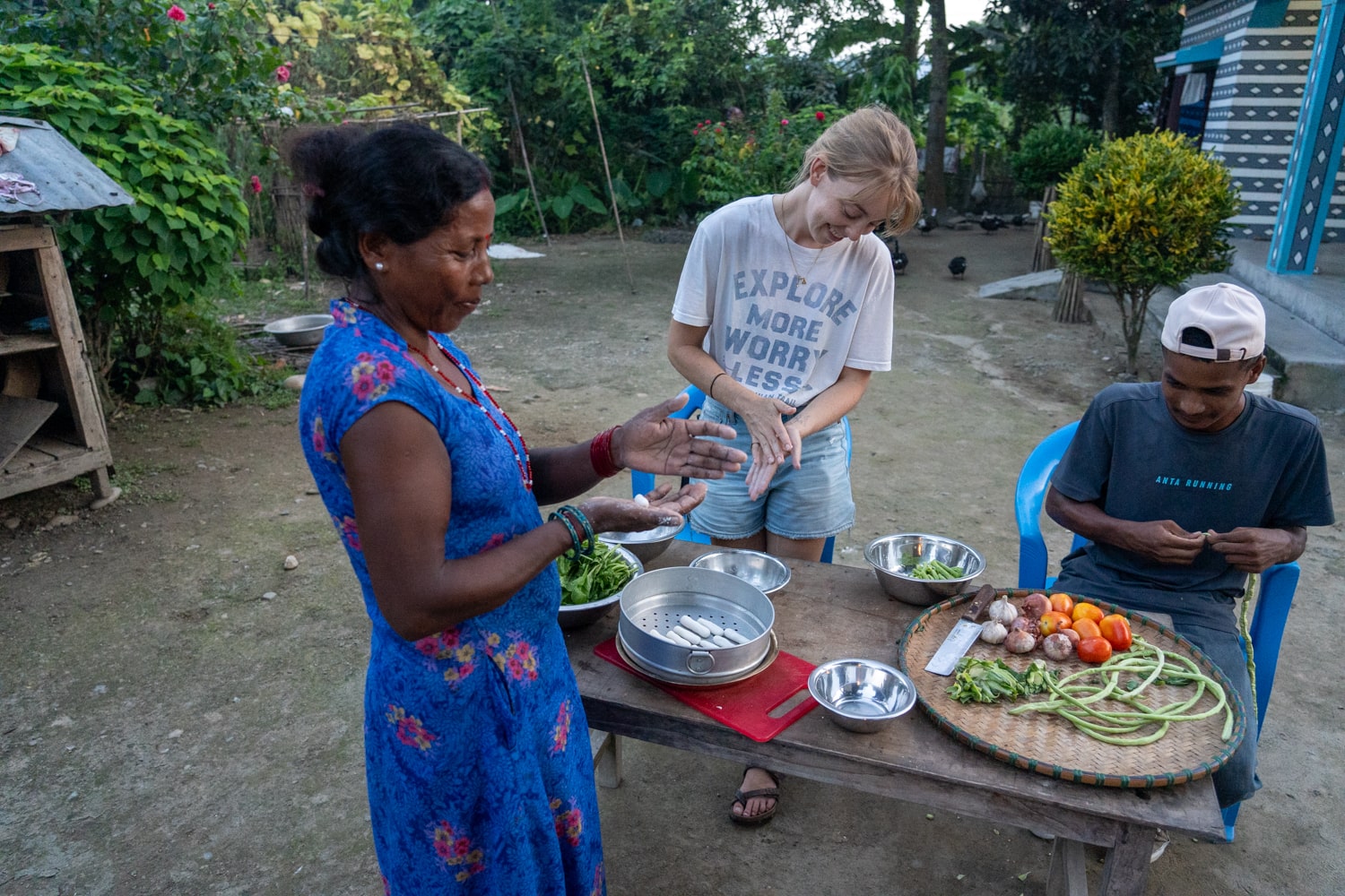 A female tourist and local Tharus prepare food together outside.