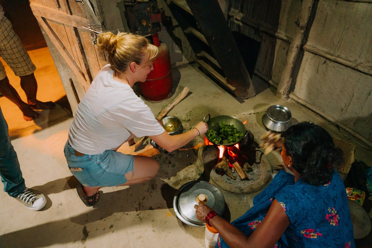 A female traveler cooks with local Tharu woman inside home for a homestay in Chitwan.