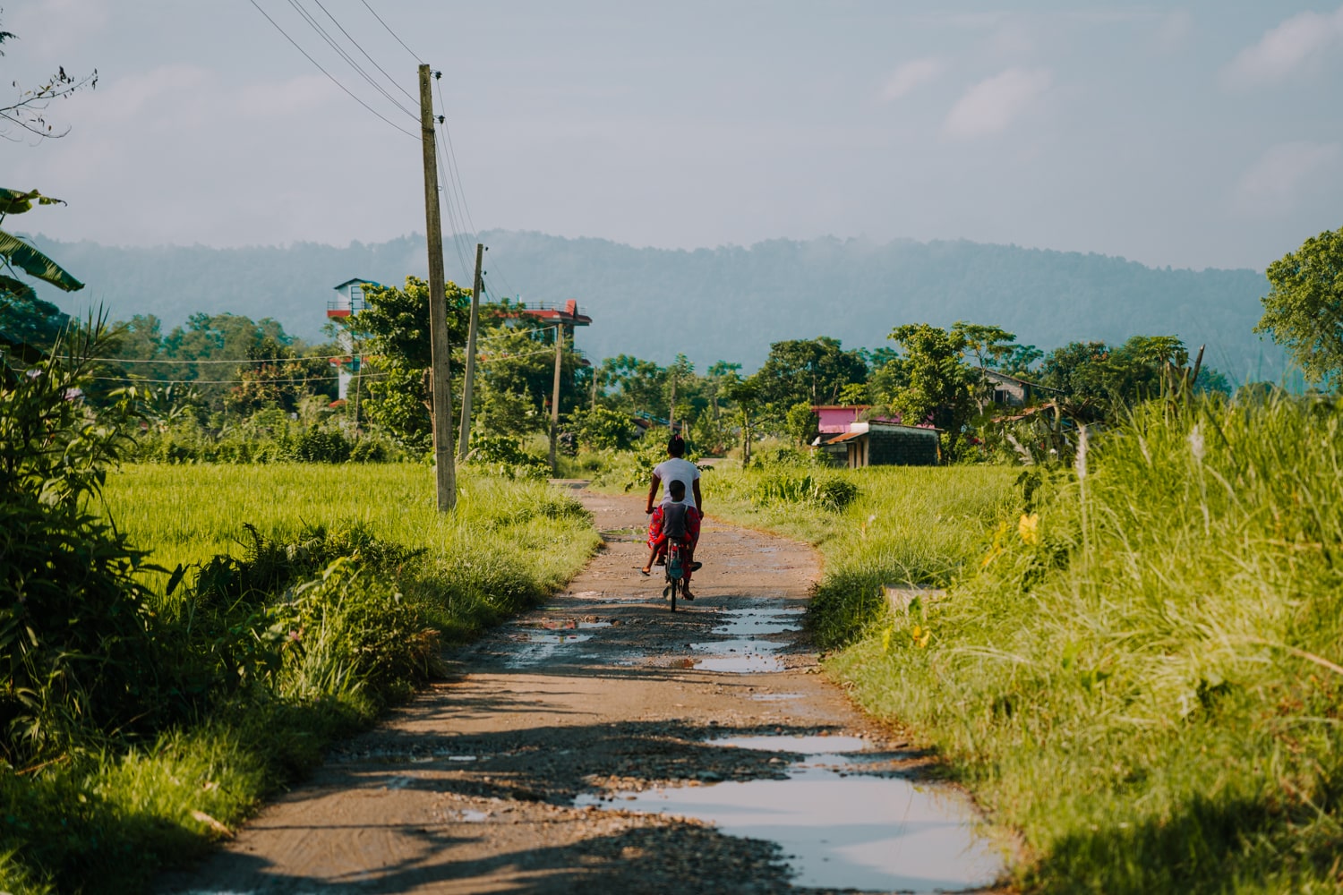 Local Tharu woman and child riding a bike down a dirt road in Barauli, Chitwan.