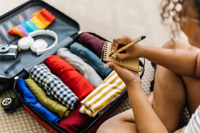 Mixed race young adult woman writing list of accessories and travel stuff before going on summer holidays