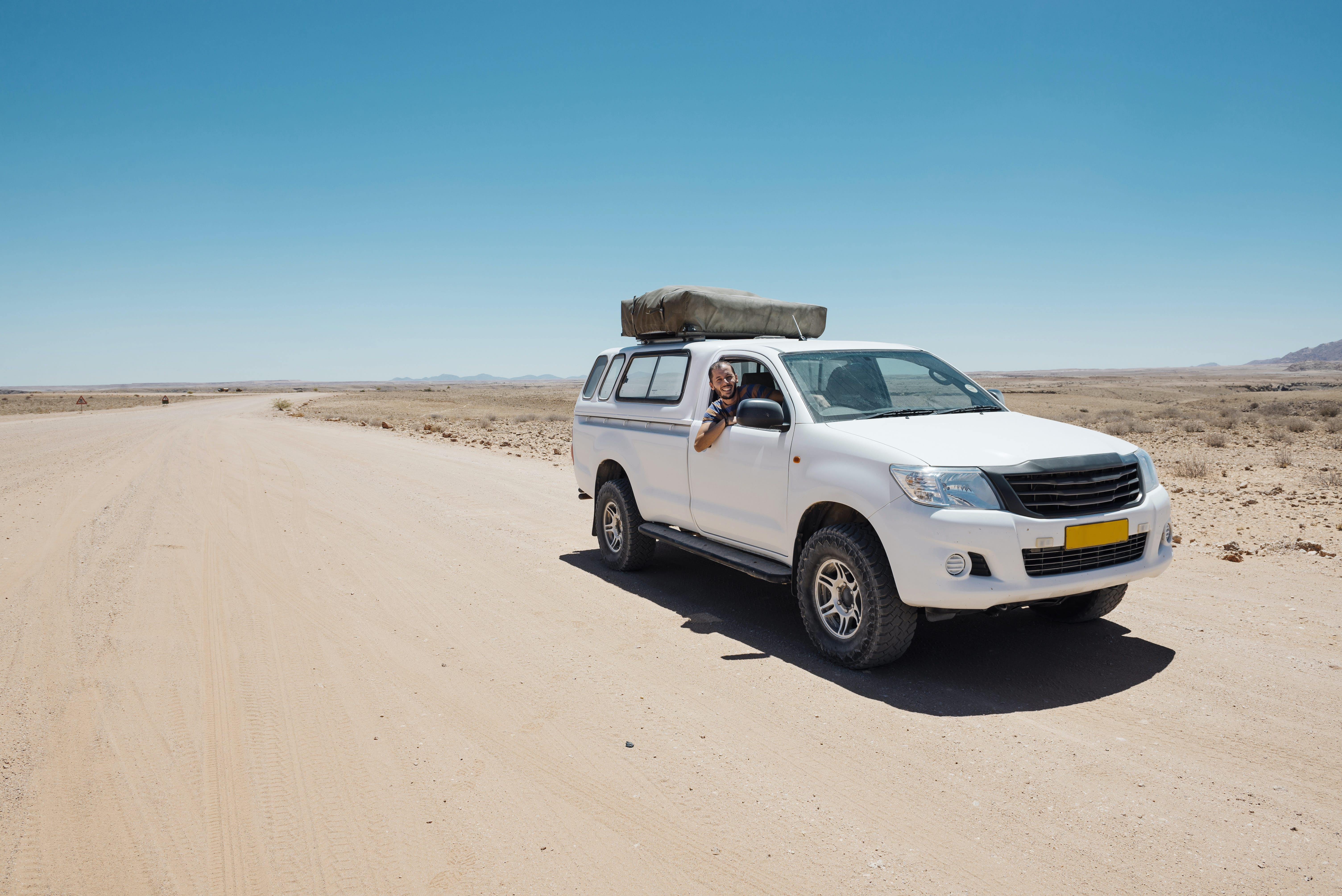 Man in a four-wheel drive car with a tent on the roof parked on a dusty desert road