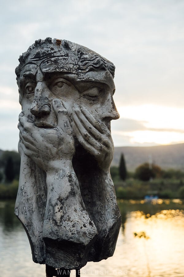 A sculpture with four faces against sunset on the lake inside Rustavi Park.