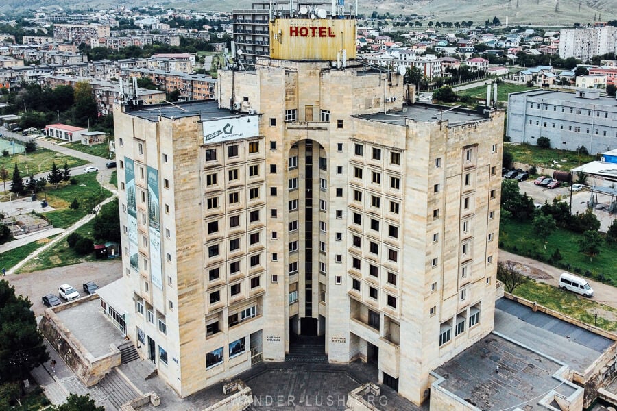 A drone photo of the Hotel Rustavi, a Brutalist building in the country of Georgia faced with yellow sandstone.