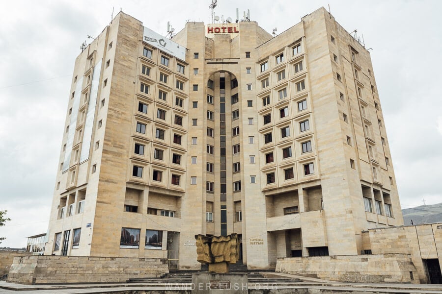 The facade of the Soviet Hotel Rustavi, with a sculpture and fountain in front.