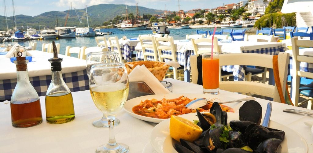 On the front beach, there is a table, a wine glass, a glass of juice, two plates of seafood, and two bottles of condiments. 