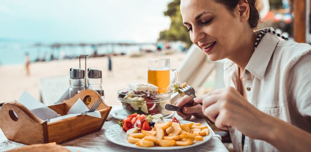 Beautiful young woman eating food in the restaurant at the beach on a sunny day. 