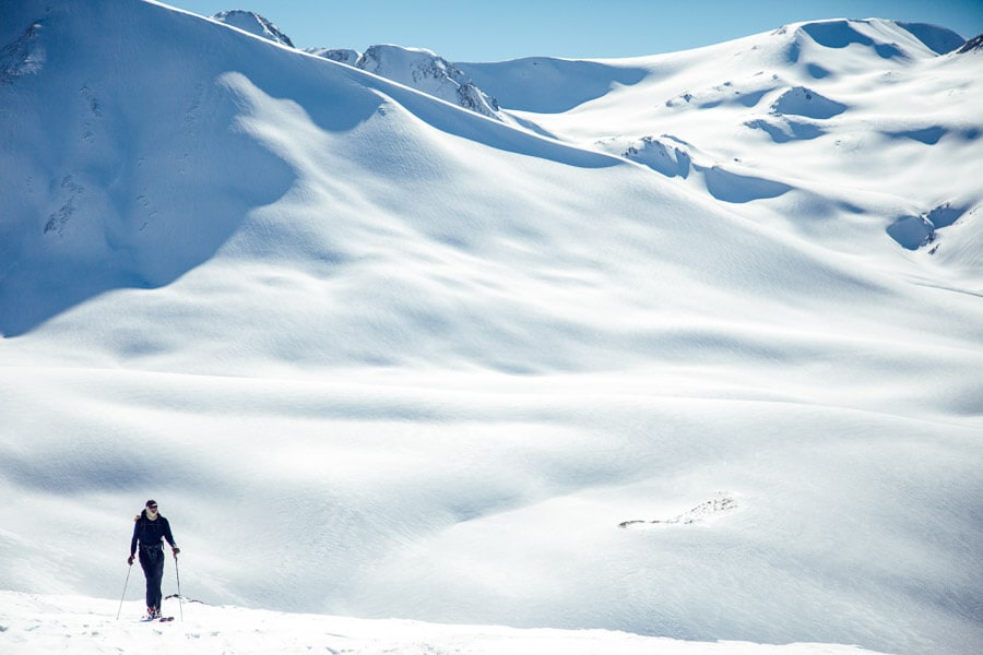 A lone skier walks across a field of snow in the shadow of a tall mountain whilst skiing in India at Gulmarg Resort.