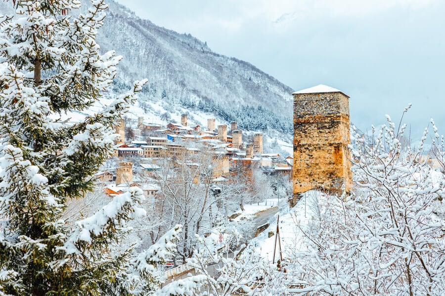 Ancient tower houses in Svaneti, Georgia against a backdrop of snowy hills.