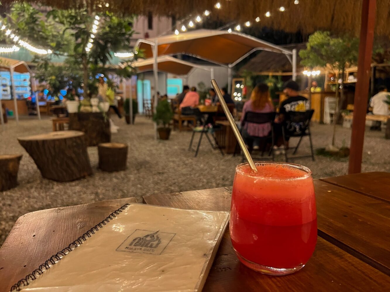 A glass of watermelon juice and menu sit on a table outdoors at Malaya Café in Nepal.