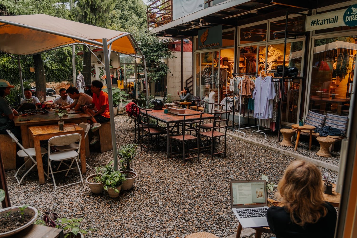 A cozy courtyard in Kathmandu with friends drinking and digital nomads working on their laptops at the coffee shop.