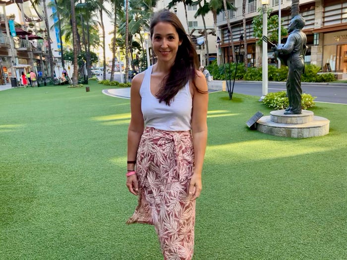 A woman stands for a picture in front of a green lawn and shopping area wearing a tropical print skirt.