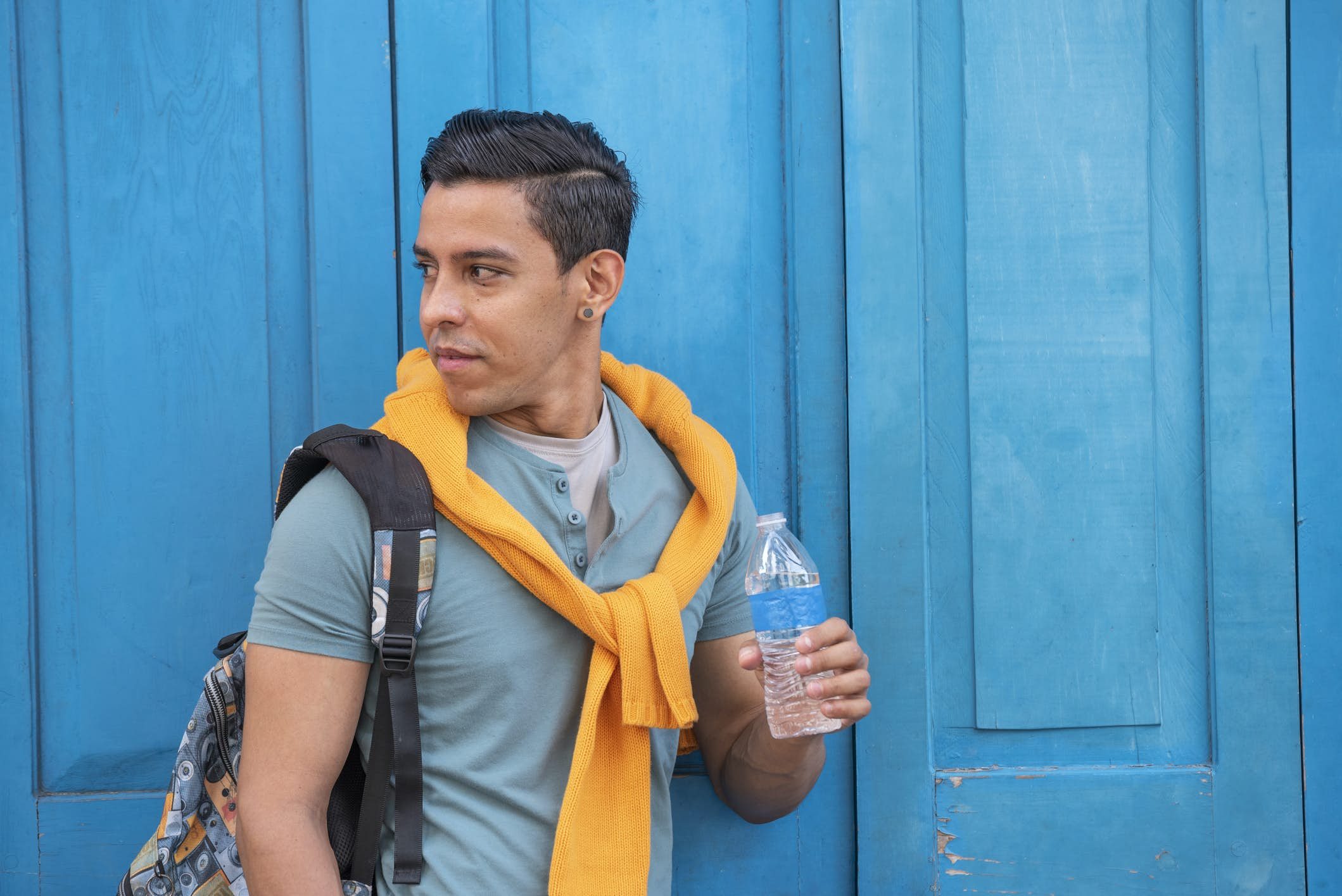 Young hispanic men with a bottle of water standing by a blue door, Panama