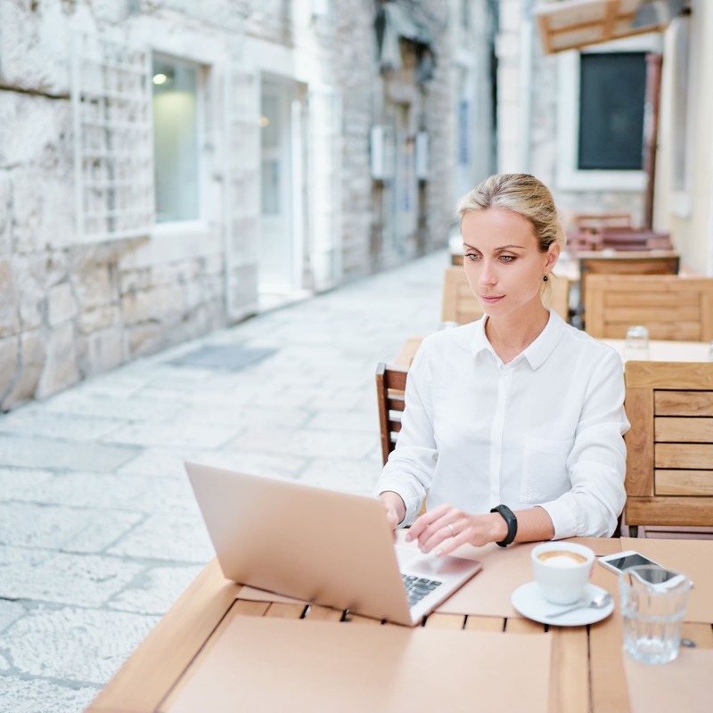 Young Blonde Remote Worker Wearing A White Shirt As She Types On Her Laptop While Sitting At An Alfresco Cafe In Split, Croatia, Digital Nomad