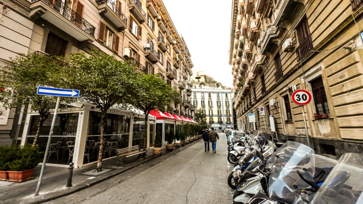 A row of motorcycles parked on a bustling Naples city street.