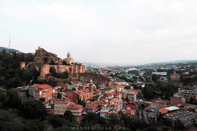 The city of Tbilisi viewed from above, with a stone fortress and colourful houses.