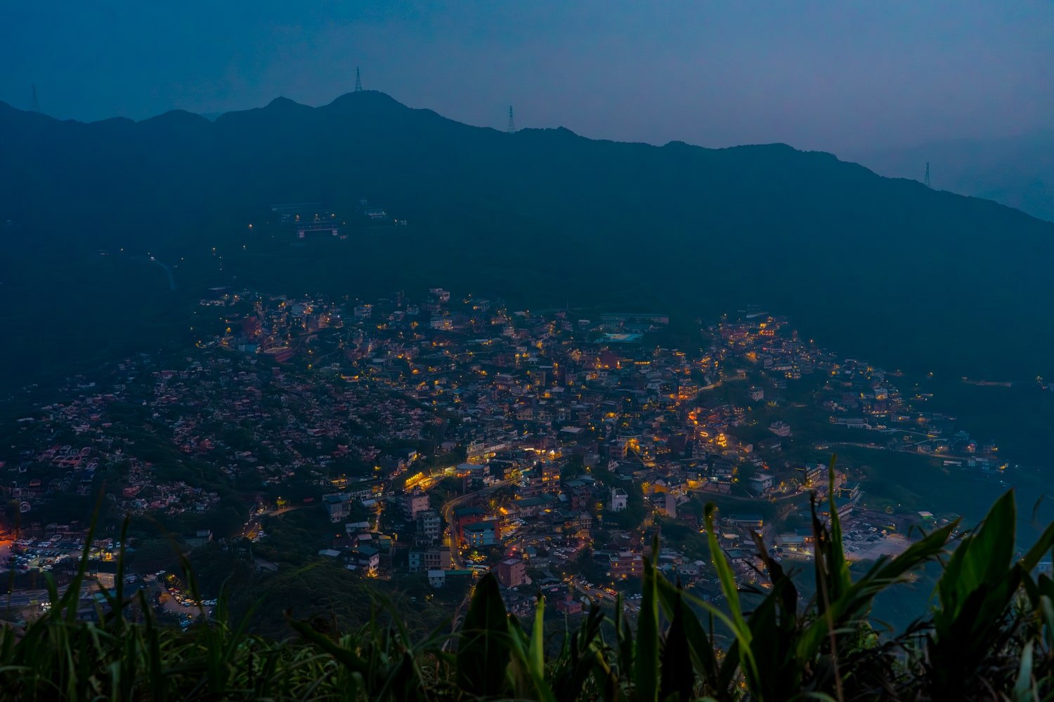 Night scene of Jiufen mountain village in Northern Taiwan illuminated by town evening lights and passing traffic.