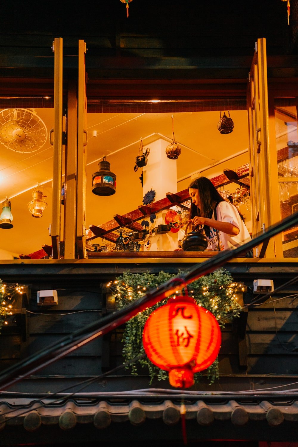 Woman inside a teahouse in Jiufen, Taiwan with decorations and evening lights.