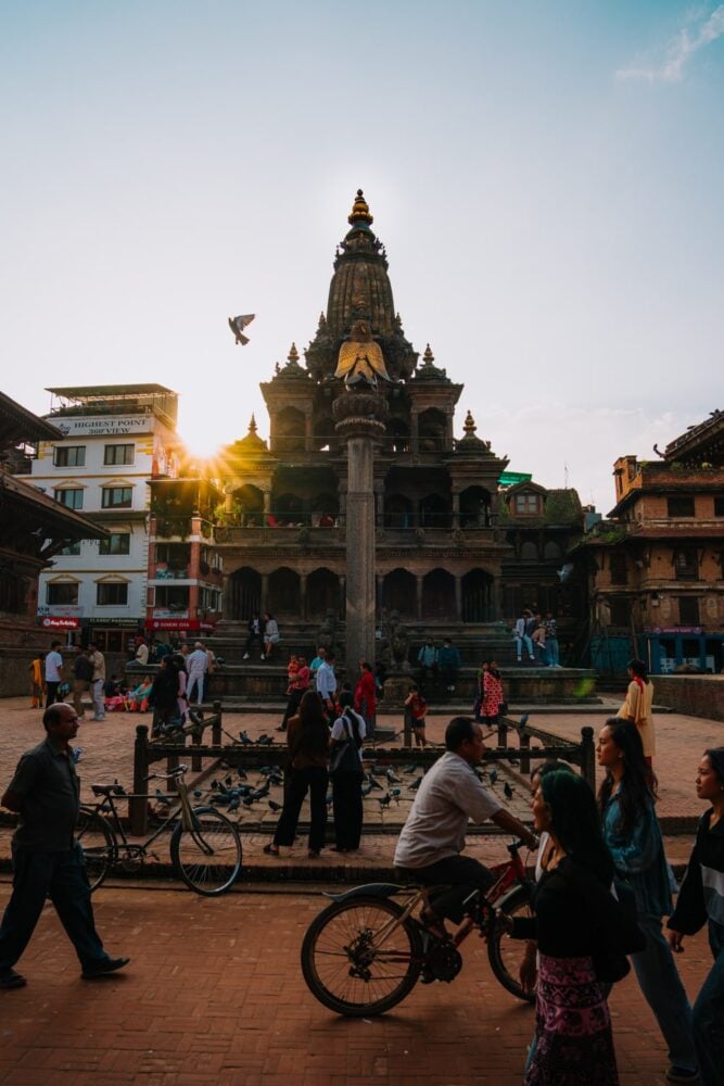 Sunset behind Krishna Mandir temple with pedestrians and crowd in front.