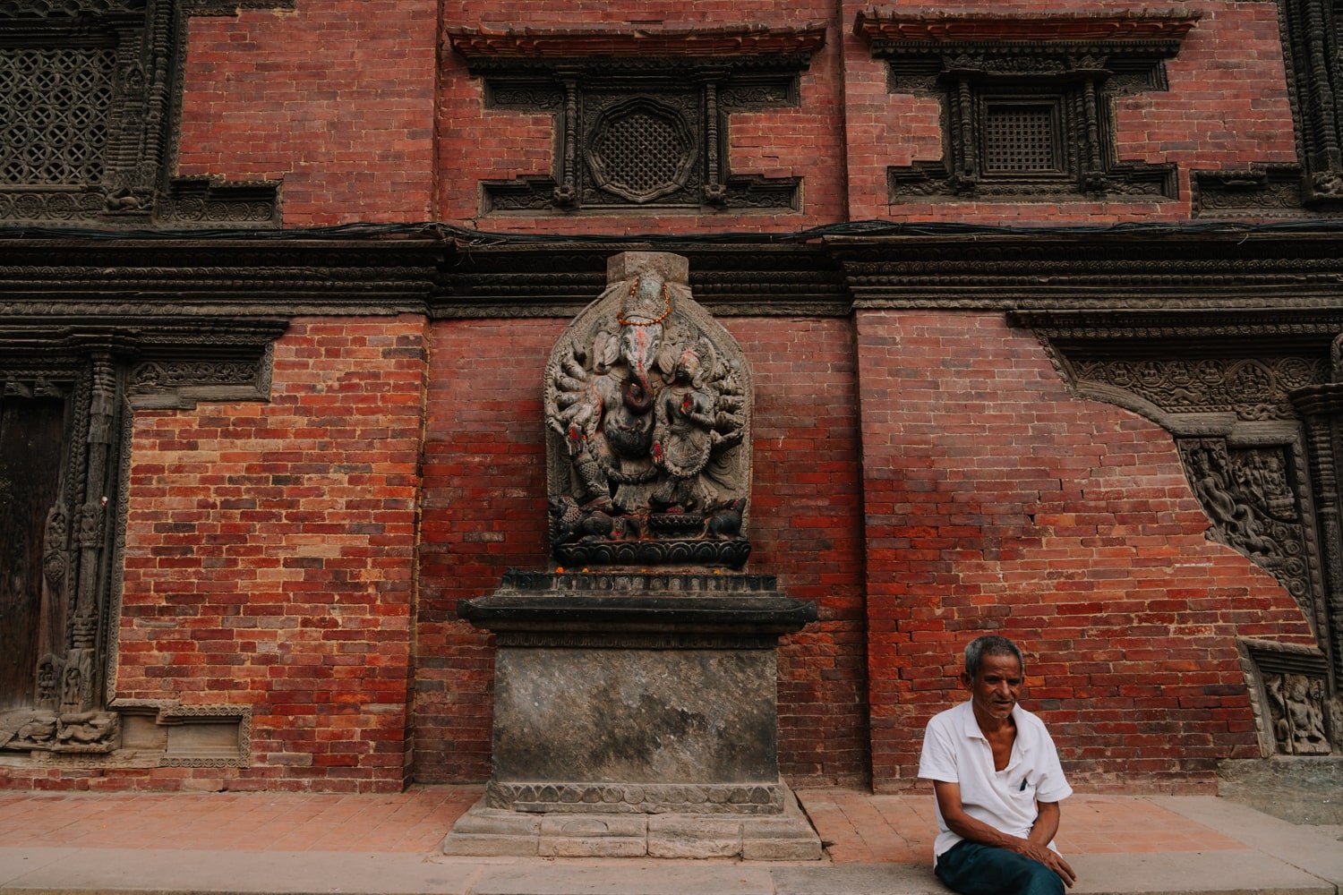 A man sits on ledge in front of a Ganesh statue in Patan Durbar Square.