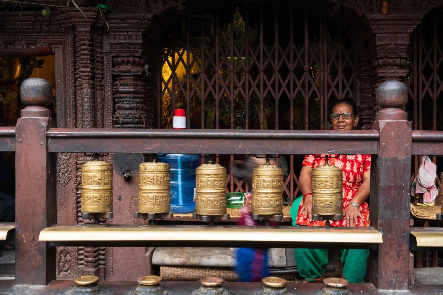 A Nepali woman sits behind a row of golden prayer flag wheels at the Golden Temple in Patan Durbar Square, Lalitpur.