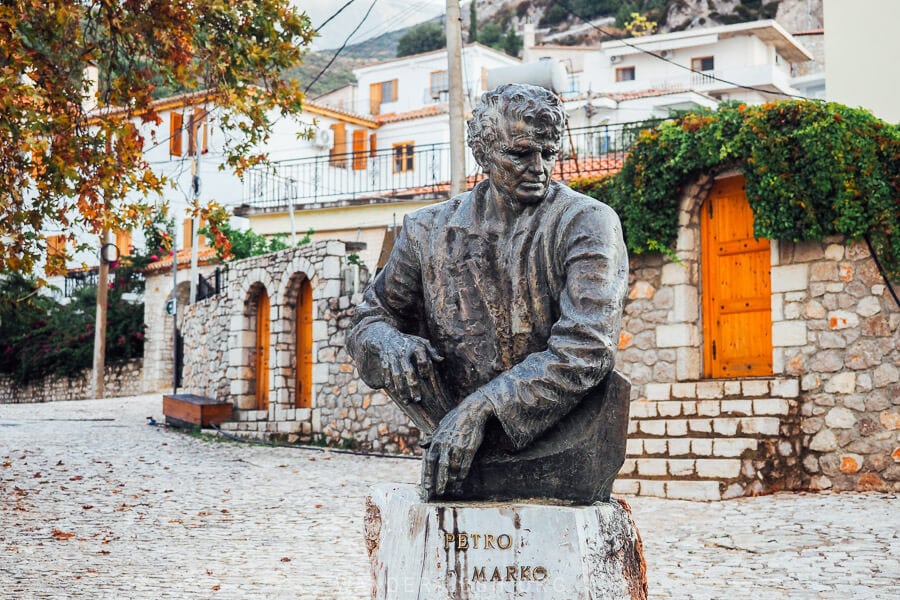 A statue of Albanian author Petro Marko stands in front of heritage houses in Dhermi.