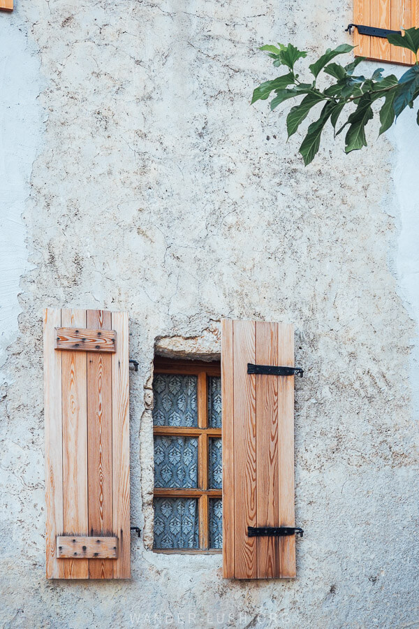 A small window with wooden shutters on the side of an old house in Dhermi, Albania.