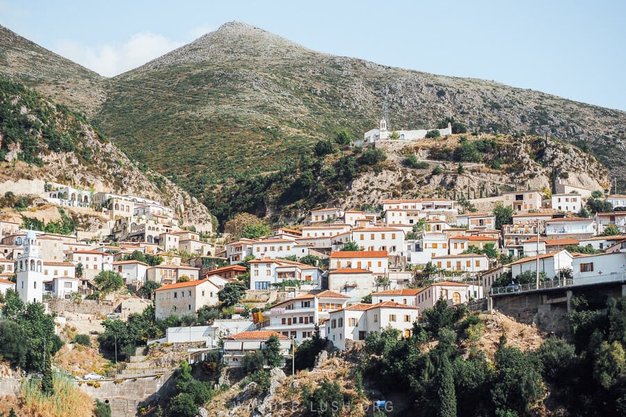 A view of Dhermi from the highway, with white houses stacked on the mountainside and a monastery in the middle distance.