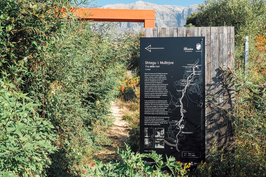 A black information board provides directions for the Mills Trail, a historic walking route from Dhermi village to the beach.