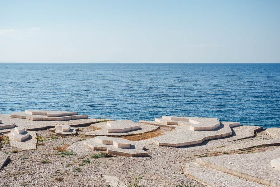 A sculptural ensemble on the waterfront in Dhermi, with the blue sea just beyond.
