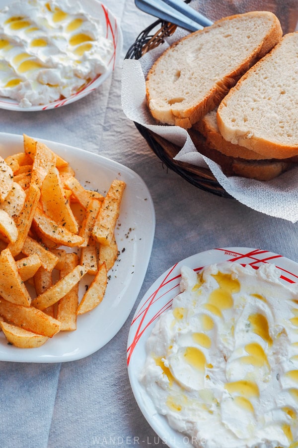 Two plates of tzatziki and a bowl of fries on a white table at a cafe in Dhermi, Albania.