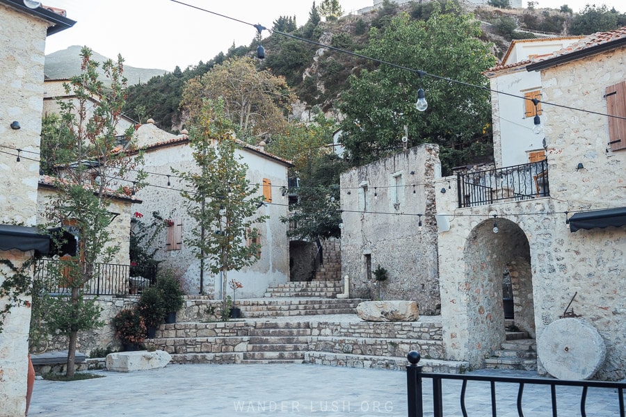 A small square in Dhermi surrounded by heritage stone buildings and with an old mill stone propped up against a wall.