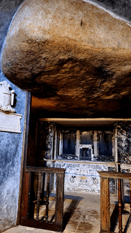 A large stone boulder forms the ceiling in the chapel at the Convent of the Capuchos, and a stone altar sits at the front of the room