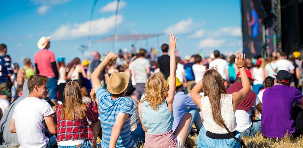 Group of teenagers at a summer music festival, sitting on the grass in front of the stage. 