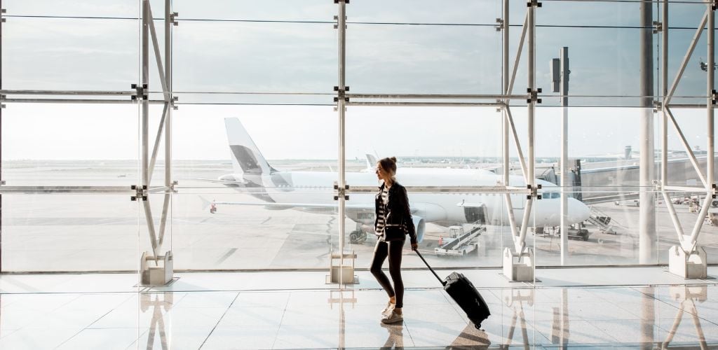 View on the airport window with woman walking with suitcase at the departure hall of the airport.