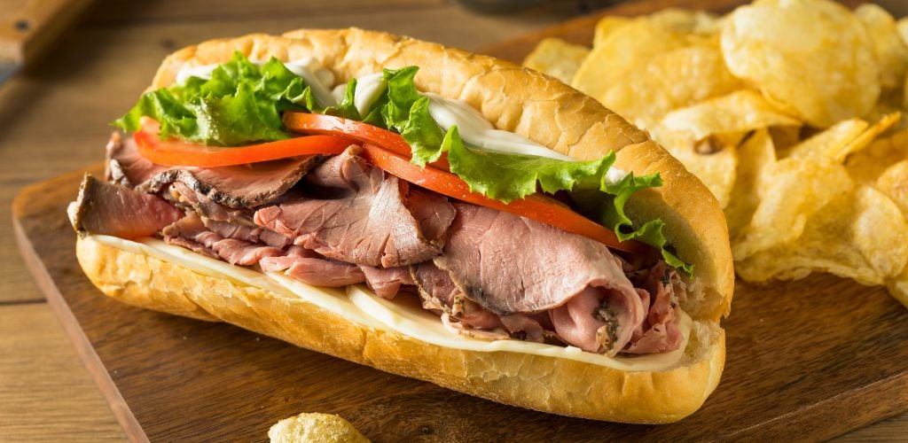 Homemade Roast Beef Deli Sandwich with Lettuce and Tomato. Potato chips on the background. 