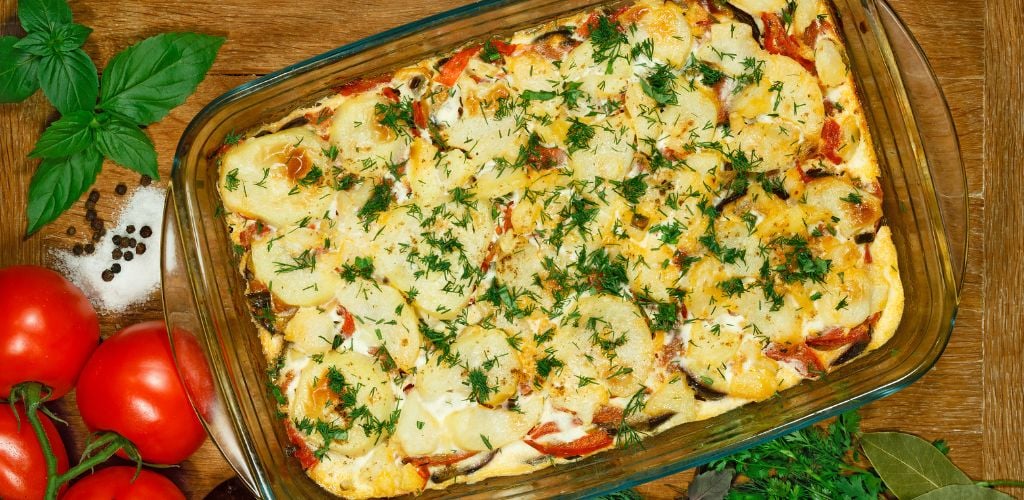 Vegetarian moussaka. Traditional Greek dish. Casserole with eggplants, aubergine, potatoes, tomatoes, garlic, egg, yogurt, onions, nutmeg, and oregano. Transparent glass baking dish. 