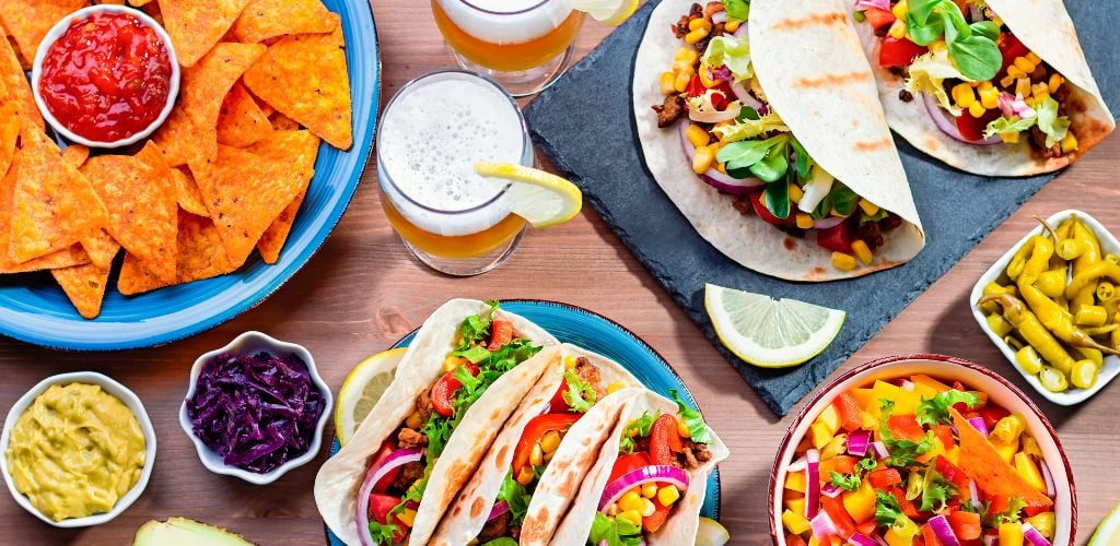 Table with tacos, mango salsa, nachos with sauce, guacamole, lemon beer and appetizers and traditional mexican dishes on wooden table. 