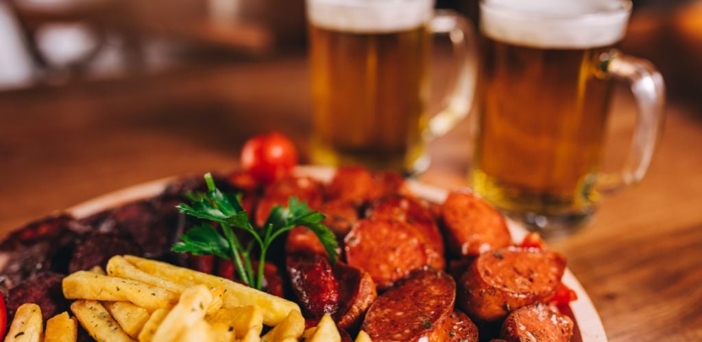 A platter of fries and sliced sausage. Two glasses of beer. 