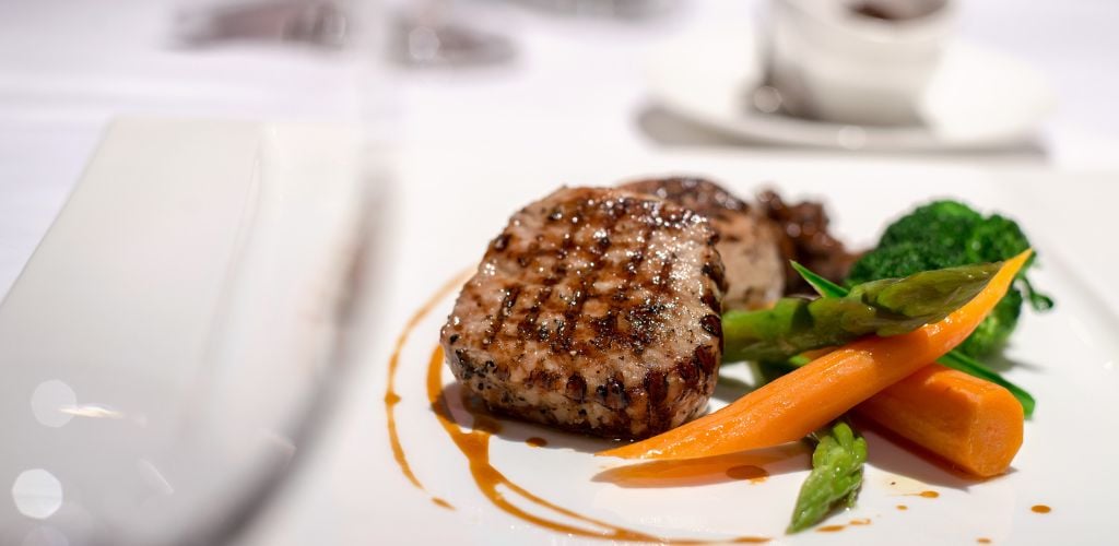 In a fine dining restaurant, a beef steak is served with asparagus, broccoli, and carrots as side dishes.  