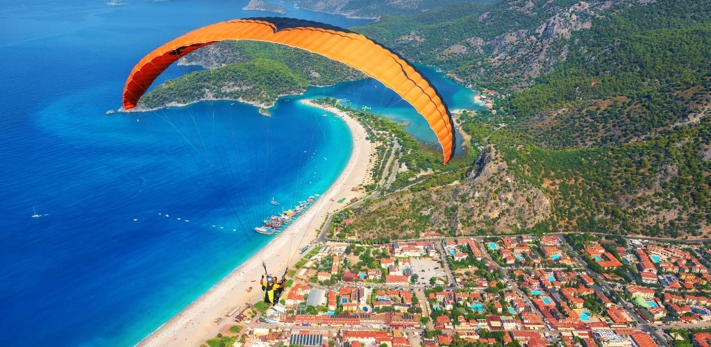 Paragliding in the sky. Paraglider tandem flying over the sea with blue water and mountains in bright sunny day. Aerial view of paraglider and Blue Lagoon in Oludeniz, Turkey. Extreme sport. Landscape