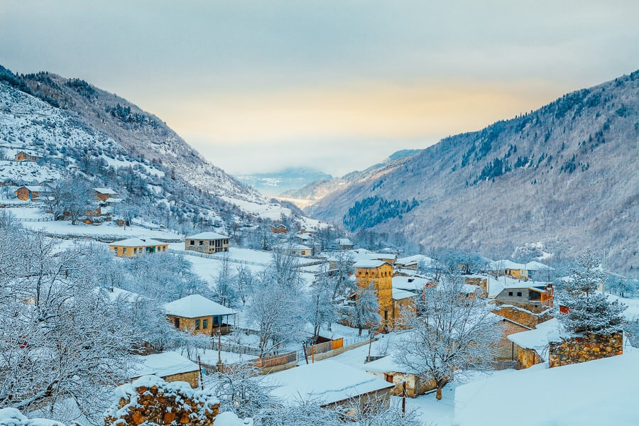 Snow covered Svaneti village with tower houses and high mountains.