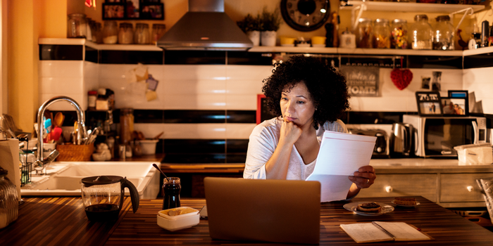 A photo of a middle-aged woman working on her finances on a laptop at her kitchen table.