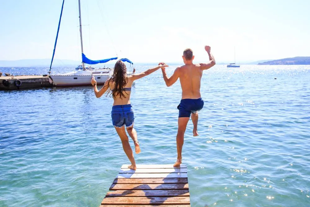 Young couple jumping off boardwalk into sea together — Getty Images