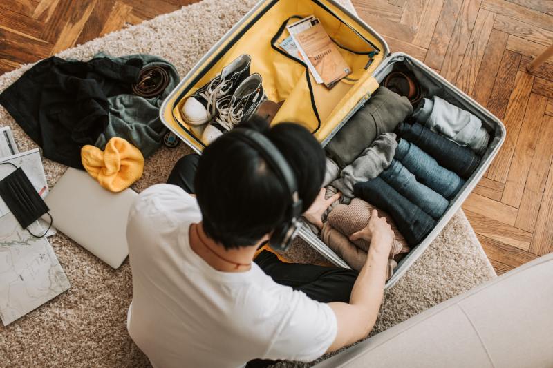 Top view of a man wearing headphones while packing a suitcase with clothing