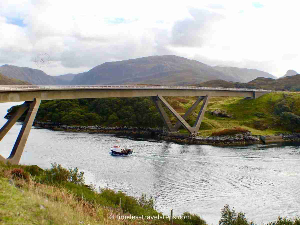 a tour boat from Kylesku harbour passing beneath the iconic Kylesku bridge on an autumn's day viewed from the viewing point by the road above the loch