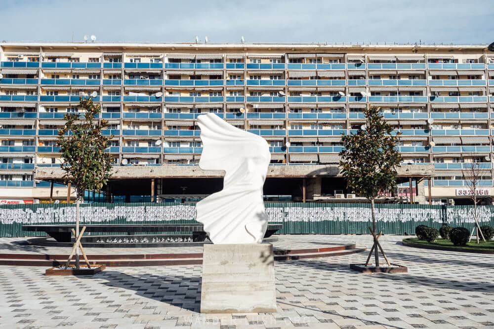 Resistance, a white stone sculpture on Avlabari Square in Tbilisi, with a blue apartment block in the background.