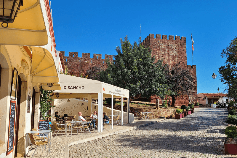 Silves Castle at the end of a cobbled street, past a cafe