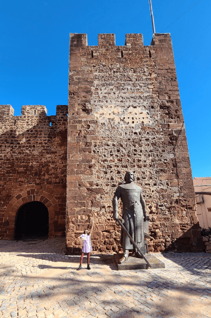 Silves brick tower with knight statue in front and child with play knight toys beside it