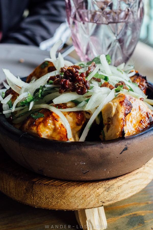 Chicken served in a clay pot and topped with onions and barberries.