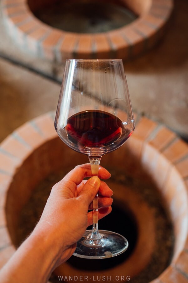 A woman holds a glass of red Imeretian wine in front of a qvevri at a winery near Kutaisi, Georgia.